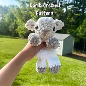 May include: A handmade crochet lamb with a fluffy white body and gray accents on the ears, hooves, and face. The text "Lamb Crochet Pattern" and "PDF download only!" are displayed on the image. The lamb is held in front of a green background.