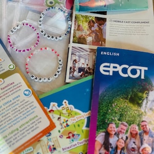 Könnte beinhalten: Eine Sammlung farbenfroher Armbänder mit weißen Buchstabenperlen mit der Aufschrift "DCP", "CAST MEMBER" und "MAGIC MAKER". Das Bild enthält auch Broschüren und Karten, darunter einen "EPCOT" -Führer und eine Themenparkkarte.