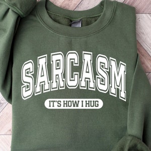 May include: A green sweatshirt with white text that reads "SARCASM IT'S HOW I HUG".