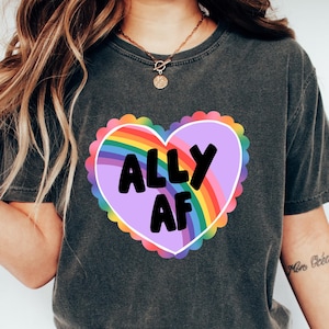 Puede incluir: Una camiseta gris oscuro con un gráfico de corazón morado con un arcoíris y el texto "ALLY AF".