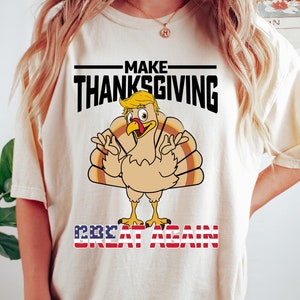 May include: A beige t-shirt with a cartoon turkey wearing a blonde wig and the text "Make Thanksgiving Great Again" with an American flag design.