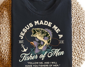 Peut inclure: T-shirt noir avec un graphique d'un poisson et le texte "Jésus m'a fait un pêcheur d'hommes" avec le verset biblique Matthieu 4:19. Le texte dit également "Suivez-moi, et je ferai de vous des pêcheurs d'hommes."