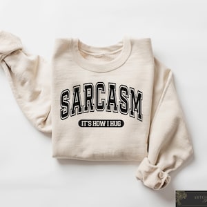 May include: A beige sweatshirt with black text that reads "SARCASM IT'S HOW I HUG".