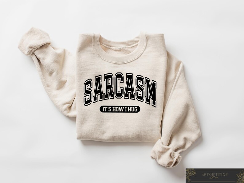 May include: A beige sweatshirt with black text that reads "SARCASM IT'S HOW I HUG".