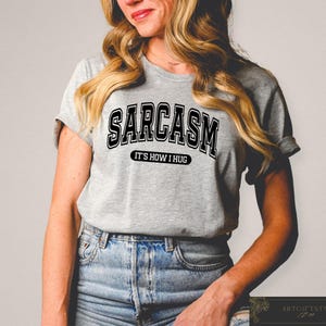 May include: A gray t-shirt with black text that reads "Sarcasm It's How I Hug".