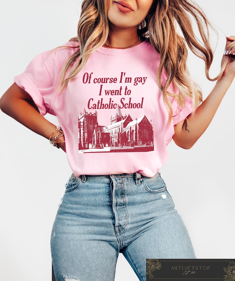 May include: Pink t-shirt with a red graphic of a church and the text "Of course I'm gay I went to Catholic School."