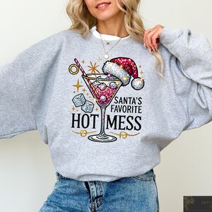 May include: Gray sweatshirt with a sparkly red and white martini glass design. The text on the sweatshirt reads "Santa's Favorite Hot Mess".