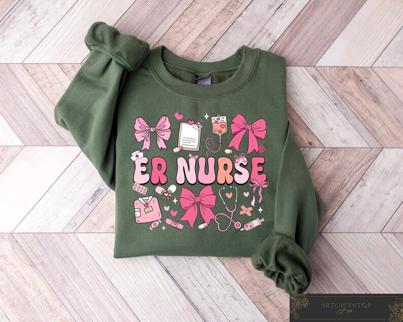 May include: Green sweatshirt with a pink and white graphic design that says "ER Nurse". The graphic includes hearts, bandages, a stethoscope, and other medical symbols.