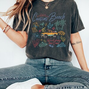 May include: Dark gray t-shirt with the words "Cousins Beach" and beach-themed illustrations. The shirt features a yellow truck, palm trees, and the text "We will always have Summer."