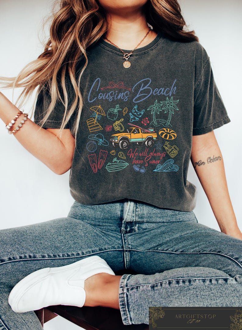 May include: Dark gray t-shirt with the words "Cousins Beach" and beach-themed illustrations. The shirt features a yellow truck, palm trees, and the text "We will always have Summer."