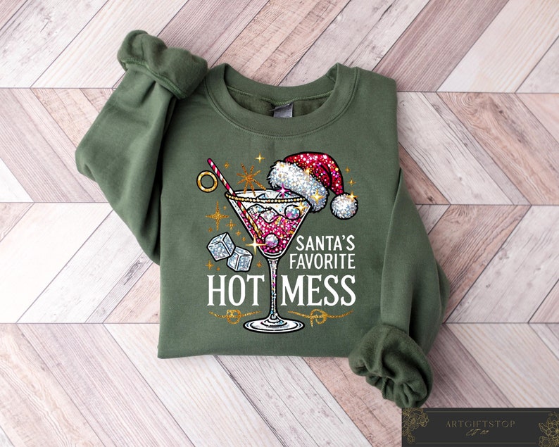 May include: Green sweatshirt with a festive design featuring a martini glass with a red drink, ice cubes, and a straw. The text "Santa's Favorite Hot Mess" is printed on the sweatshirt.