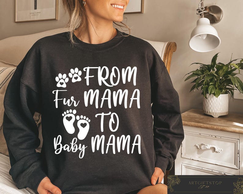 May include: Black sweatshirt with white text that reads "FROM Fur MAMA TO Baby MAMA". The design includes paw prints and baby footprints with hearts. The sweatshirt is a casual style.