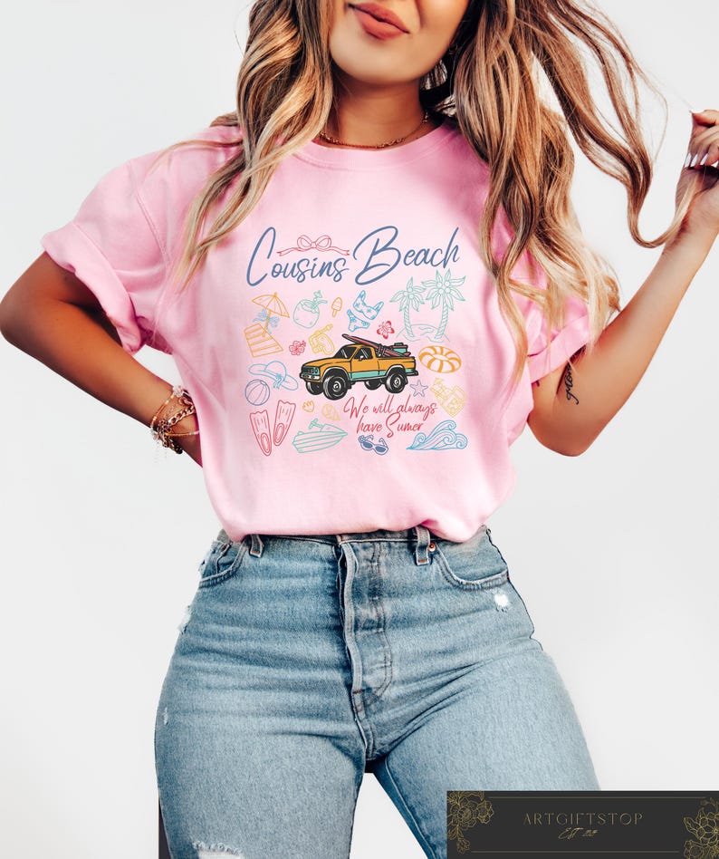 May include: Pink t-shirt with the words "Cousins Beach" and a graphic of a yellow truck carrying a surfboard, surrounded by beach-themed illustrations. The text "We will always have summer" is also included.