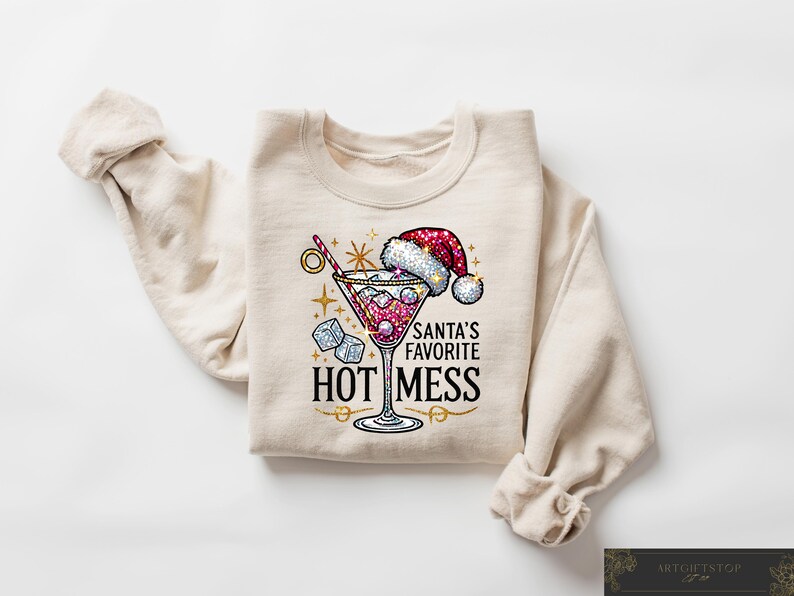 May include: A beige sweatshirt with a festive design featuring a martini glass with red liquid and ice cubes, a Santa hat, and the text "Santa's Favorite Hot Mess".