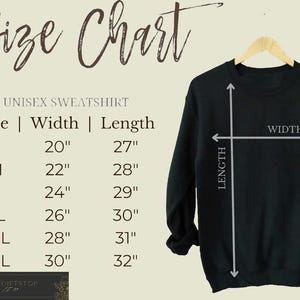 Op de afbeelding: Een zwart unisex sweatshirt op een houten hanger, met een maattabel aan de linkerkant. De tabel toont maten S tot 3XL, met breedte- en lengtematen in inches. De afmetingen van de sweatshirt worden met pijlen aangegeven.