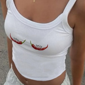 Puede incluir: Camiseta blanca de tirantes con gráficos de chiles rojos y el texto "extra spicy" en la parte delantera.