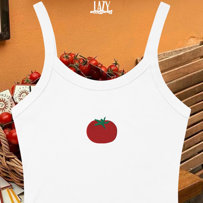 Pu&ograve; includere: Canotta bianca con spalline sottili e grafica di pomodoro rosso. La canotta ha uno scollo tondo e una silhouette aderente. La grafica del pomodoro &egrave; ricamata con foglie verdi. La parola "LAZY" &egrave; stampata in alto.