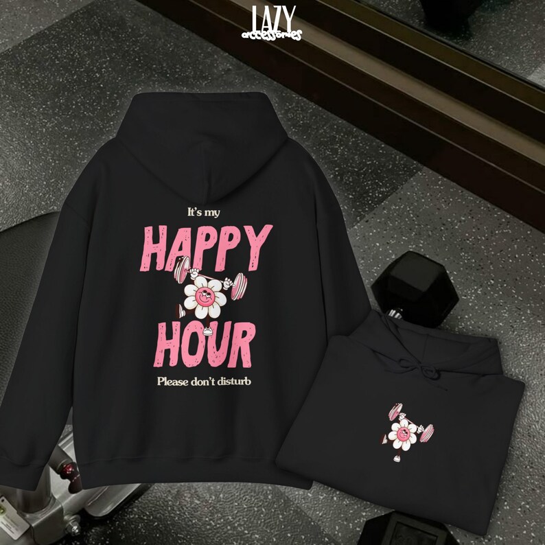 May include: Black hoodie with the text "It's my HAPPY HOUR" in pink, featuring a flower lifting weights. The phrase "Please don't disturb" is below. A second hoodie with the same design is also visible.