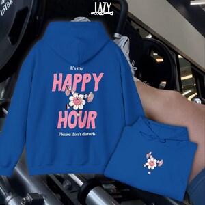 May include: A royal blue hoodie with the text "It's my HAPPY HOUR" in pink, featuring a flower lifting weights. The phrase "Please don't disturb" is below. A second hoodie is visible.