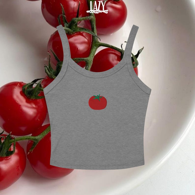 Pu&ograve; includere: Canotta grigia con grafica di pomodoro rosso. La canotta ha spalline sottili e scollatura rotonda. La parola "LAZY" &egrave; stampata in bianco in alto. I pomodorini rossi sono sullo sfondo.