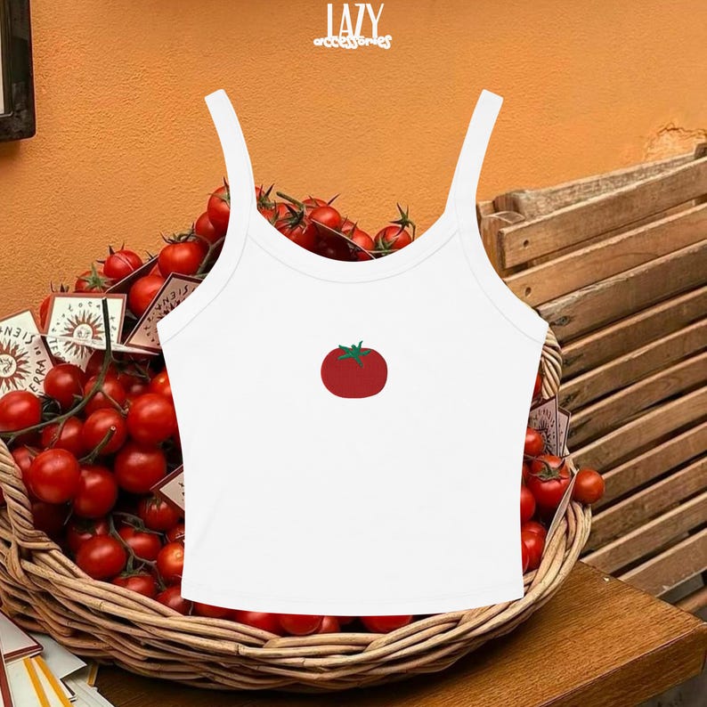 Pu&ograve; includere: Canotta bianca con spalline sottili con grafica di pomodoro rosso. La canotta &egrave; esposta davanti a un cesto di pomodori rossi. La parola "LAZY" &egrave; stampata nella parte superiore dell'immagine.