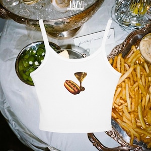 Puede incluir: Camiseta blanca de tirantes con un gráfico de un perrito caliente y una copa de martini. La camiseta es de estilo crop.