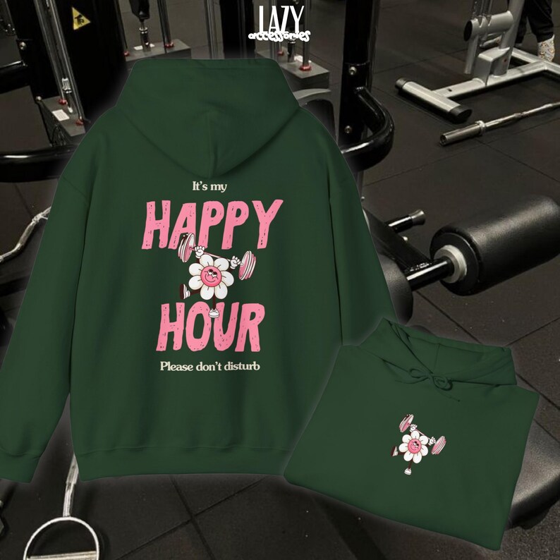 May include: Dark green hoodie with the text "It's my HAPPY HOUR" in pink, featuring a flower graphic lifting weights. The phrase "Please don't disturb" is below. A second hoodie is folded below the main one.