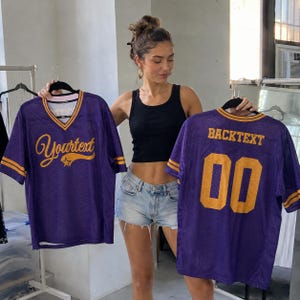 May include: Two purple mesh jerseys with yellow accents. The front jersey features the text "Yourtext" in yellow cursive with a star graphic. The back jersey displays the text "BACKTEXT" in yellow block letters above the large yellow number "00".