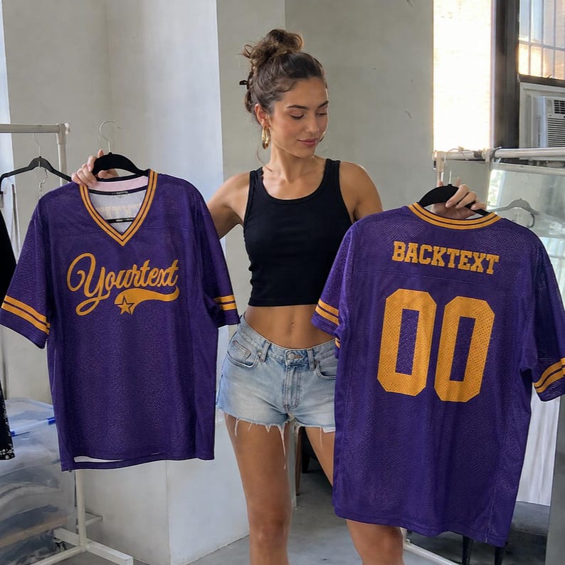 May include: Two purple mesh jerseys with yellow accents. The front jersey features the text "Yourtext" in yellow cursive with a star graphic. The back jersey displays the text "BACKTEXT" in yellow block letters above the large yellow number "00".