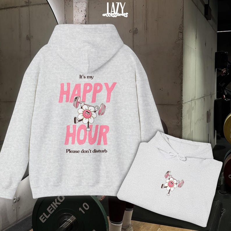 May include: A light gray hoodie with a drawstring hood and a kangaroo pocket. The back features the text "It's my HAPPY HOUR" in pink, with a flower lifting weights graphic. The phrase "Please don't disturb" is below.