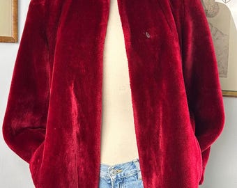 May include: A red faux fur jacket with a stand-up collar and long sleeves. The jacket is open in the front and has a slightly cropped length.