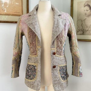 May include: A brown tweed jacket with a patchwork design featuring floral patterns. The jacket has a collar, long sleeves, and two pockets.