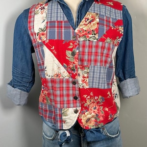 May include: A red, blue, and white patchwork vest with floral patterns. The vest has a button-up front and is made of a variety of fabrics.