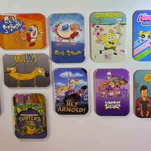 May include: A collection of rectangular magnets featuring cartoon characters from popular animated television shows. The magnets display characters from shows like "Ren & Stimpy," "SpongeBob SquarePants," and "The Powerpuff Girls."