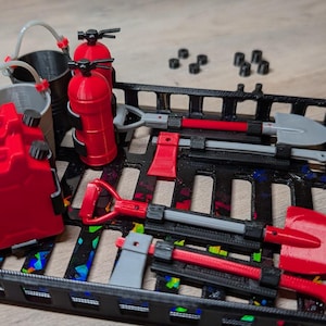 May include: A collection of miniature firefighting tools, including shovels, axes, a water tank, fire extinguishers, and buckets, all arranged in a black tray. The tools are primarily red, gray, and black, with a few small black pieces scattered around.