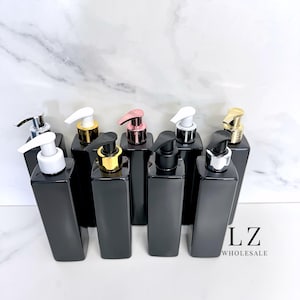 Peut inclure: Huit flacons carrés noirs avec des pompes de couleurs différentes. Les flacons sont disposés en rangée sur une surface en marbre blanc. Le texte "LZ WHOLESALE" est visible dans le coin inférieur droit de l'image.