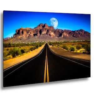 May include: A landscape wall art print featuring a long, straight asphalt road with double yellow center lines leading toward a massive, rugged mountain range under a deep blue sky with a large, bright full moon visible above the peaks.
