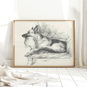 May include: A charcoal sketch print in a light wood frame depicting a German Shepherd dog resting on a tufted armchair. The dog is lying down with its head propped on the armrest, rendered in shades of black, gray, and white on a cream background.