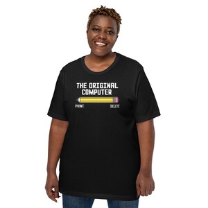 Peut inclure: T-shirt noir avec l'inscription blanche "THE ORIGINAL COMPUTER". En dessous, un crayon jaune avec une gomme rose et les mots "PRINT" et "DELETE". Le t-shirt est à col rond.