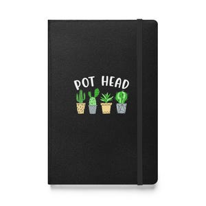 May include: Black notebook with the text "POT HEAD" in white, above four potted cacti illustrations. The notebook has a black elastic band closure.