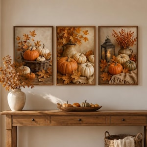 May include: A wooden console table with three drawers, topped with a ceramic vase of autumn branches and a wooden bowl of pumpkins. Above the table hang three framed prints depicting pumpkins, autumn leaves, and lanterns. A woven basket sits below.
