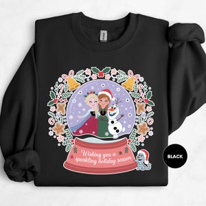 A black sweatshirt with a colorful illustration of two girls and a snowman on a Christmas-themed background.