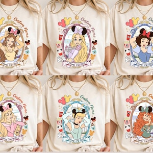 May include: Cream-colored t-shirts featuring Disney princesses in oval frames. Each princess wears a Minnie Mouse bow and is surrounded by themed graphics. Text includes "Custom Name" and "Disney Trip 2025".
