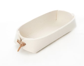 Soporte para mando a distancia con correas de cuero en color blanco crema y fieltro de lana gris.