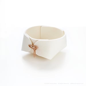 May include: A white felt basket with a unique design. The basket has a rounded shape with a folded edge and is secured with a tan leather tie. The basket is approximately 6 inches in diameter and 3 inches tall.