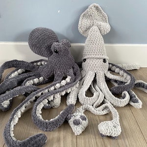 Könnte beinhalten: Zwei Plüsch-Meereskreaturen: ein grauer Oktopus und ein hellgrauer Tintenfisch. Der Oktopus hat einen runden Kopf und acht lange, sich kräuselnde Tentakel mit weißen Akzenten. Der Tintenfisch hat einen spitzen Kopf und Tentakel. Beide haben schwarze Augen.