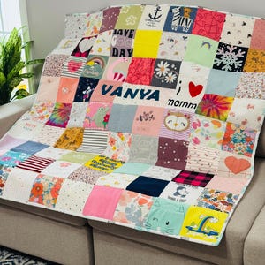 Op de afbeelding: Een handgemaakte patchworkquilt over een bank. De quilt bestaat uit verschillende stoffen vierkanten in verschillende kleuren en patronen, waaronder bloemenprints, strepen en de tekst "Vanya nommm".