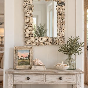 May include: A rectangular wall mirror framed with numerous natural oyster shells in shades of cream, gray, and brown. The mirror features a textured, organic border composed of overlapping shells, creating a layered and dimensional appearance.