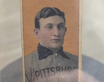 May include: Vintage baseball card featuring a portrait of a man in a Pittsburgh Pirates uniform. The card has a tan border and the team name is visible on the jersey. The player's name, Wagner, is printed at the bottom.
