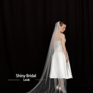 May include: A white bridal dress with a short skirt and a long, sheer veil. The veil is trimmed with small beads. The text "Shiny Bridal Look" is visible in the image. The background is black.